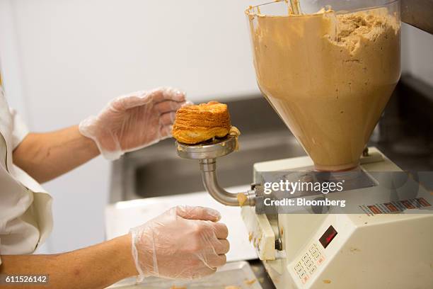 An employee uses a machine to fill a freshly made Cronut with praline-flavored butterscotch during the opening of the Dominique Ansel Bakery in...
