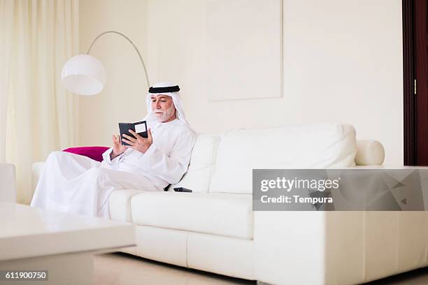 oriente medio senior en casa con el teléfono están complementadas en dishdasha.   - arab old man fotografías e imágenes de stock