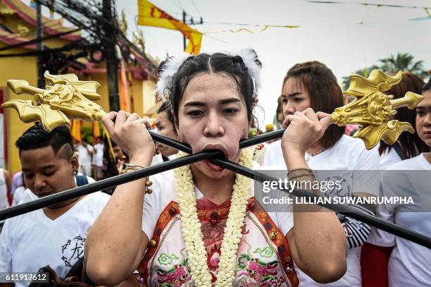 Devotee of the Nine Emperor Gods marches with large poles pierced through her cheeks during the annual Phuket Vegetarian Festival in the southern...