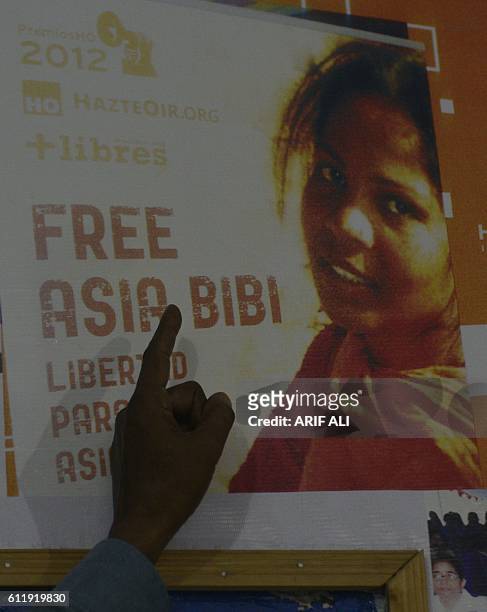 In this photograph taken on September 27 Ashiq Masih, husband of Asia Bibi, a Christian woman facing death sentence for blasphemy, points to a poster...