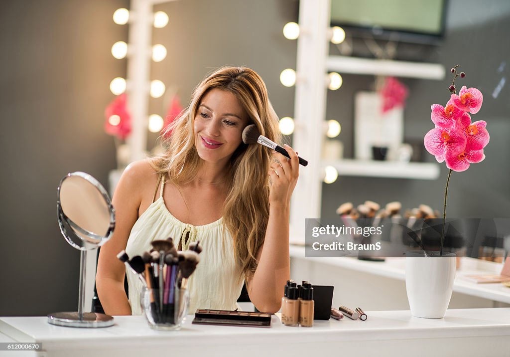 Femme heureuse appliquant de la poudre pour le visage avec une brosse de maquillage.