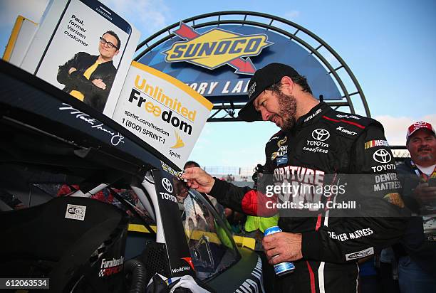 Martin Truex Jr., driver of the Furniture Row/Denver Mattress Toyota, affixes the winners decal to his car in Victory Lane after winning the NASCAR...