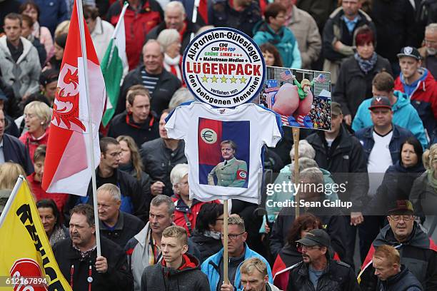 Supporters of the Pegida movement, including one holding a sign that shows German Chancellor Angela Merkel dressed in a Nazi uniform with the...