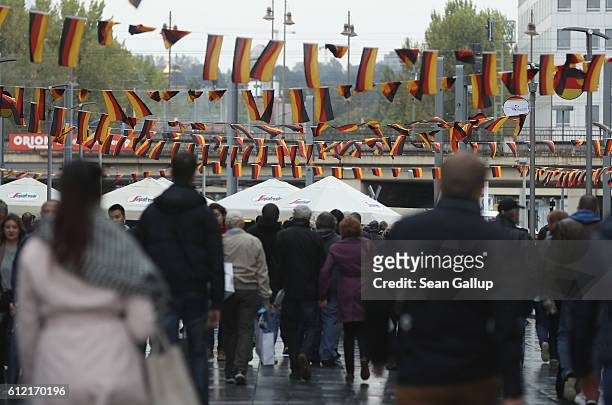 People walk under Germn flags fluttering above in the city center during celebrations to mark German Unity Day on October 3, 2016 in Dresden,...
