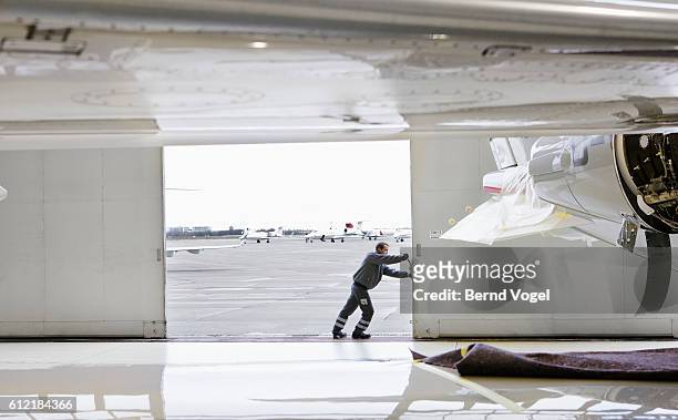 aviation worker opening hangar door - hangar stock-fotos und bilder