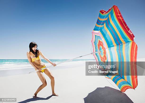 young woman unfurling umbrella on windy beach - sunshade stock pictures, royalty-free photos & images