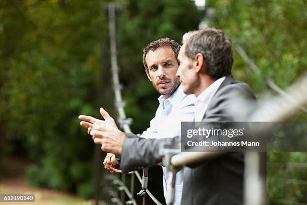 men having conversation on footbridge - hängebrücke stock-fotos und bilder