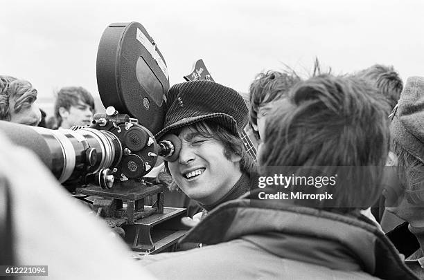 John Lennon of the Beatles pop group, looking through the lens of a camera during shooting of their new film Help! on the Salisbury Plain at Knighton...