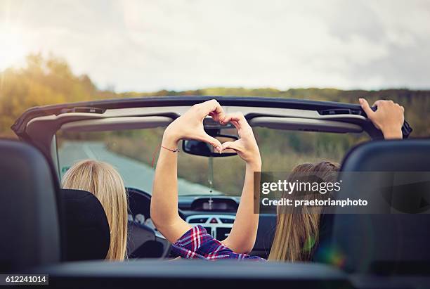 two girls in convertable making heart with their hands - car love stock pictures, royalty-free photos & images