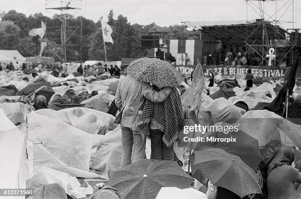 Young couple stand up to get a better view of the main stage underneath their umbrella as the rain falls. 26th June 1971.