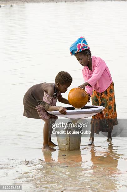 Young Ghanaian girl and her sister gather water from the dam for her family to drink and carefully filter it to guard against guinea worm disease.