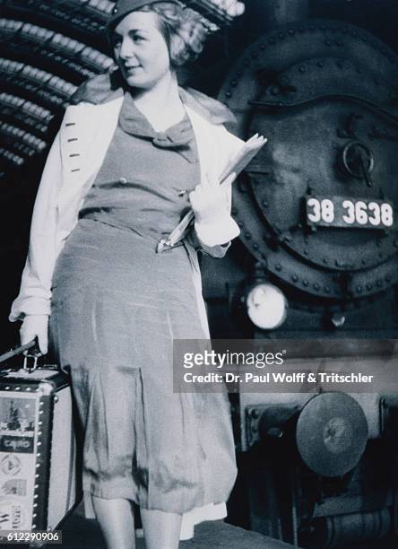 Young woman with suitcase in front of a locomotive