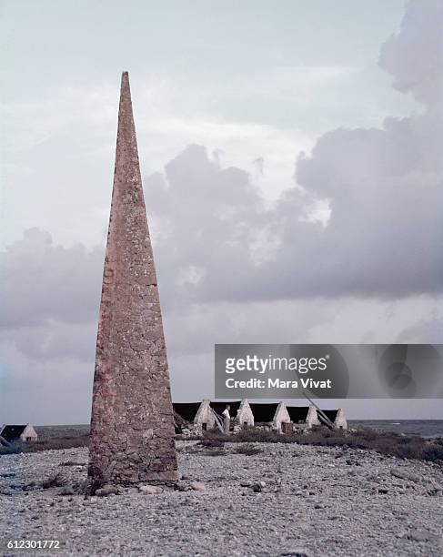 An obelisk stands on a beach beside a row of slave quarters. The obelisk directed ships to the settlement on Bonnaire. Netherlands West Indies.