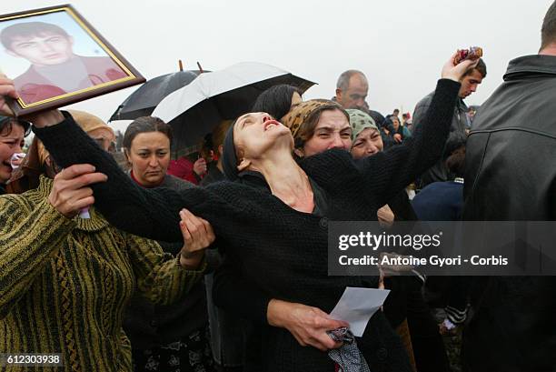 Svetlana Khoutsistova holds up a portrait of her son, Azamat, aged 26, who died in the Beslan school siege at Vladikavkaz cemetery, surrounded by...