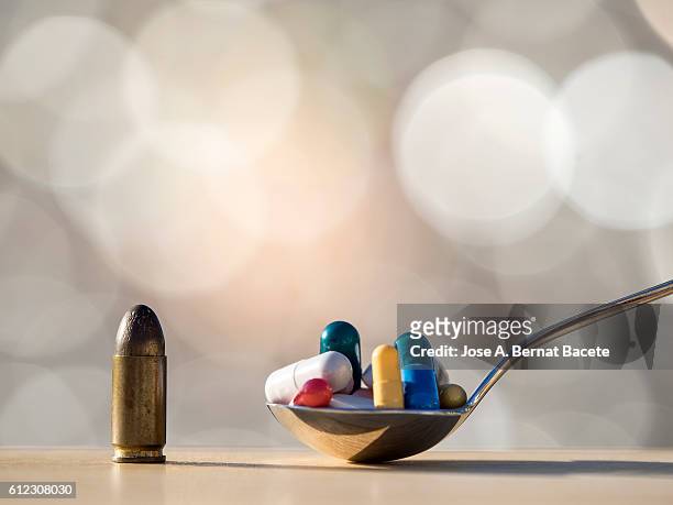 bullet of a pistol and spoon with many medicines, difficult decisions - tomada de decisão imagens e fotografias de stock