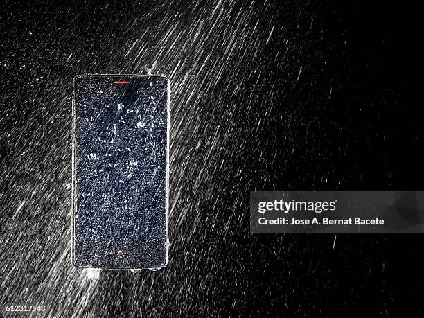 water jet striking on a wet mobile phone, on a black background - permanence stock pictures, royalty-free photos & images