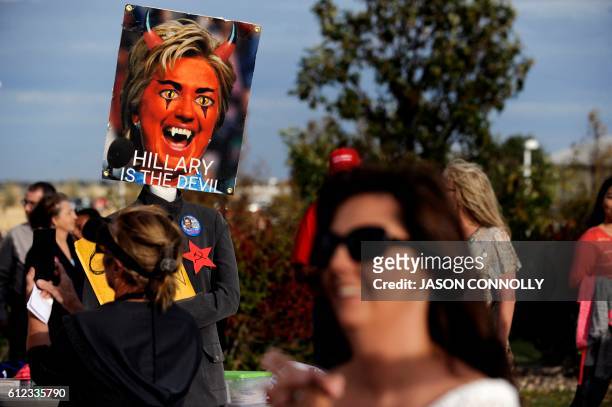 Supporters of Republican presidential nominee Donald Trump walk past an anti-Clinton poster while waiting in line to enter the Budweiser Events...