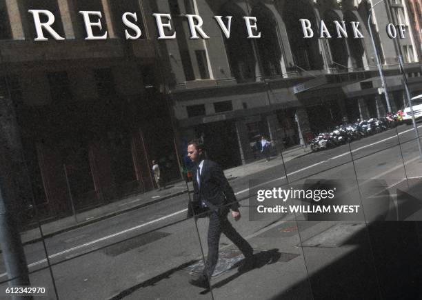 Man is reflected on a wall underneath the Reserve Bank of Australia sign in Sydney on October 4 as Australia's central bank kept interest rates at a...