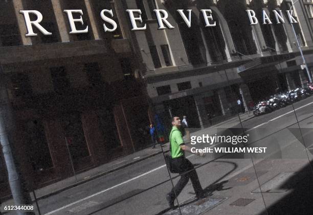 Man is reflected in a wall beneath the Reserve Bank of Australia sign in Sydney on October 4 as Australia's central bank kept interest rates at a...