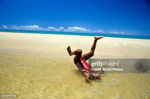 Afro-Brazilian 10-years old girl plays in a pond formed by river water in the sands of a tropical beach - black child having fun, enjoyng nature,...