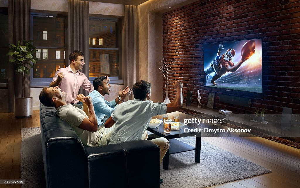 Young men cheering and watching American football game on TV