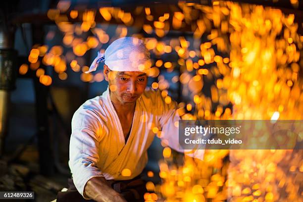 japanischer schmied schürt ein feuer, das sich darauf vorbereitet, ein schwert zu schmieden - schmied stock-fotos und bilder