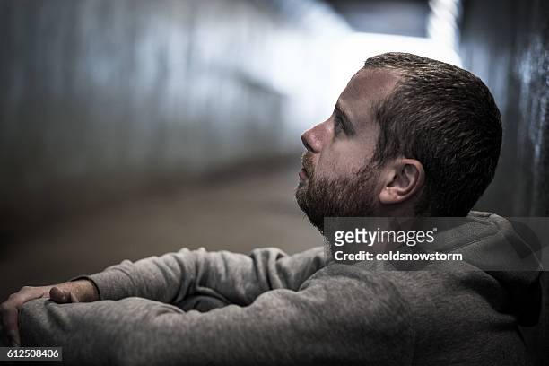 homeless adult male sitting in subway tunnel begging for money - homelessness stockfoto's en -beelden