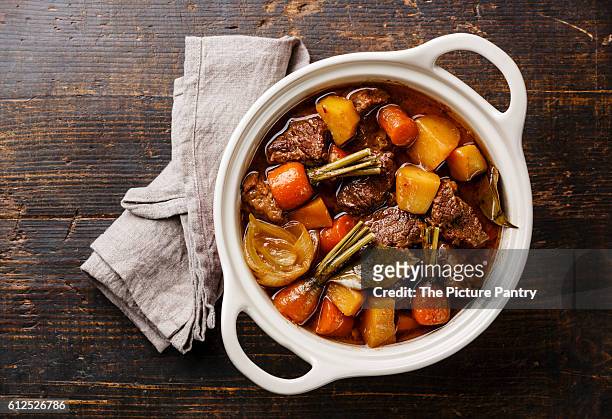 beef meat stewed with potatoes, carrots and spices in ceramic pot on wooden background - beef bourguignon stock pictures, royalty-free photos & images