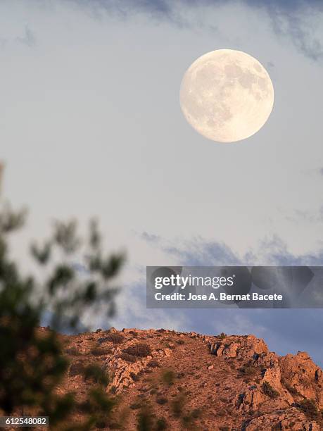 mountaintop illuminated by sunlight at sunset with bright full moon in the blue sky - moon landscape stock pictures, royalty-free photos & images