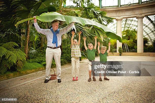 Prince Philippe with his three children, Elisabeth, Gabriel, and Emmanuel playing with a banana tree leaf in the winter garden section of the royal...