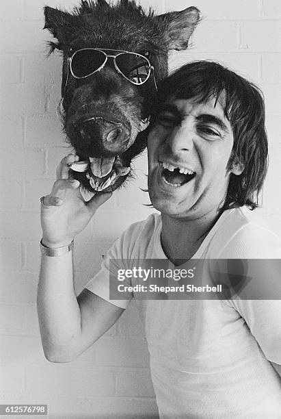 The Who's drummer Keith Moon touching a preserved warthog's head wearing aviator glasses.