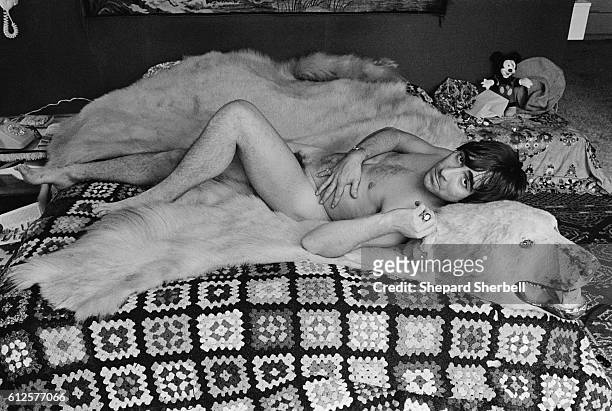 The Who's drummer Moon lying naked on a polar bear skin rug on his bed.