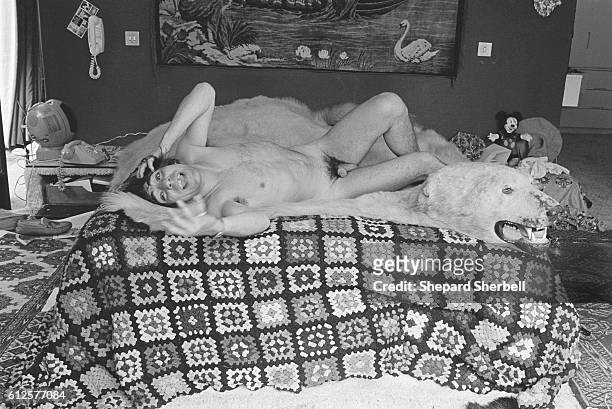 The Who's drummer Keith Moon laughing and lying naked over a polar bear skin rug on his bed.