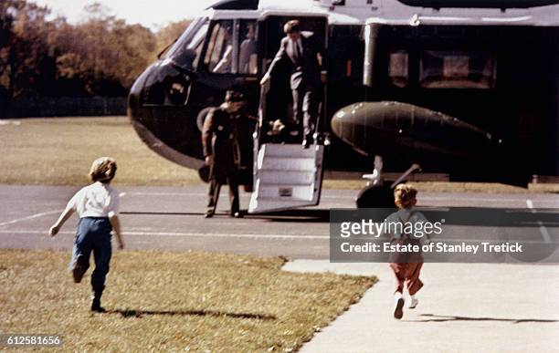 Caroline and John Jr run to welcome their father, American President John F. Kennedy, as he gets out of the helicopter.