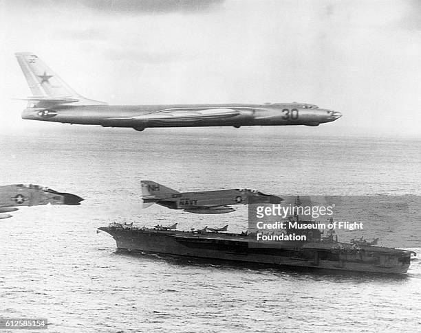 Russian-made Tupolev TU-16 Badger-A surveillance bomber flies with U. S. Navy escort fighters over the attack carrier USS Kitty Hawk during Cold War...
