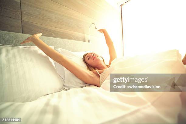 young woman waking up in her hotel room, stretching arms - woman bedroom sleeping bildbanksfoton och bilder