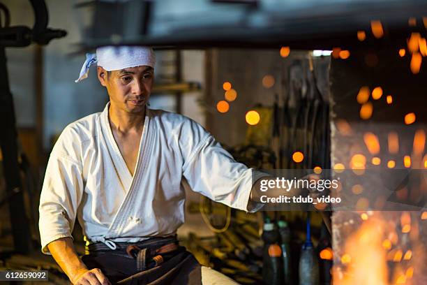 japanese blacksmith stokes a fire preparing to forge a sword - samurai sword stock pictures, royalty-free photos & images