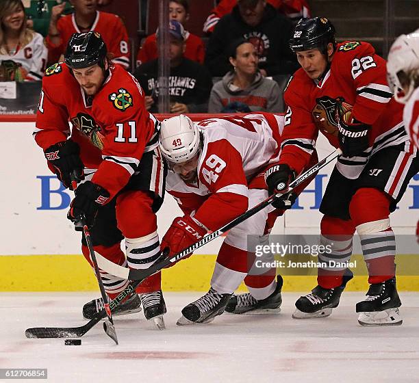 Eric Tangradi of the Detroit Red Wings tries to get to the puck between Andrew Desjardins and Jordin Tootoo of the Chicago Blackhawks during a...