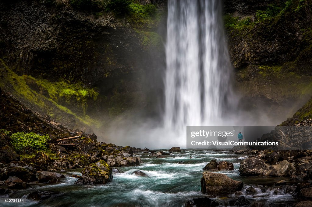 Man standing close to huge waterfall.
