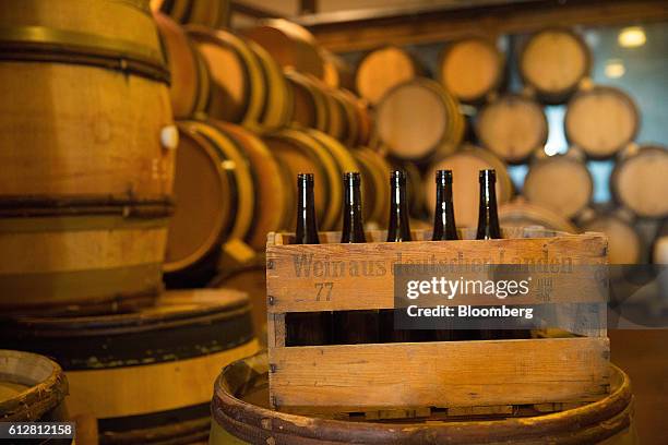 Wine bottles stand in a crate as barrels sit stacked in a temperature-controlled building inside the Weingut Friedrich Becker Estate in Schweigen,...