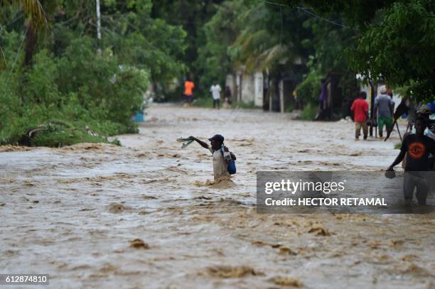 People try to cross the overflowing La Rouyonne river in the commune of Leogane, south of Port-au-Prince, October 5, 2016. - Haiti and the eastern...