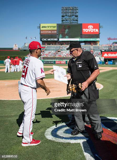 Bench coach Dino Ebel of the Los Angeles Angels of Anaheim presents umpire Bob Davidson with the lineup card as Davidson leaves the field after...