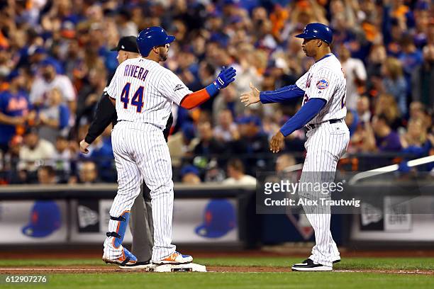 Rene Rivera of the New York Mets is greeted by first base coach Tom Goodwin after hitting a single during the National League Wild Card Game against...