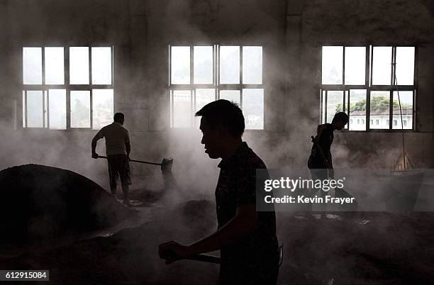 Chinese workers spread steamed sorghum on the ground as they prepare it for the first fermentation to be used in locally made wine called baijiu at...