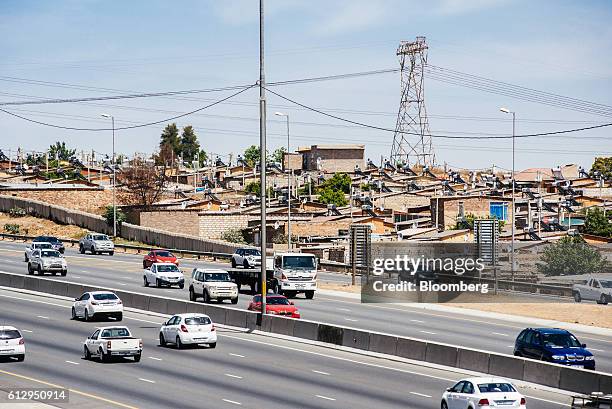 Pylon tower carries electrical power lines over residential shacks, some equipped with solar power geysers on their roofs, near a highway in the...