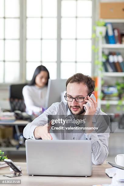 young man with eyeglasses talking on the phone at workplace - asking price stock pictures, royalty-free photos & images