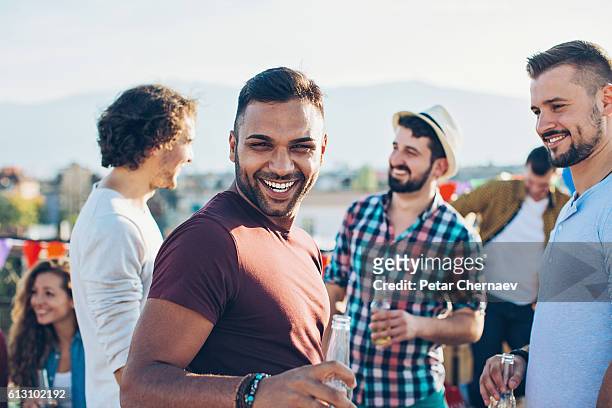 cheerful young men on a rooftop party - male friends drinking beer stock pictures, royalty-free photos & images