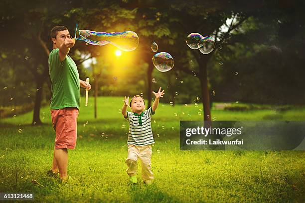 asian child playing bubble wand with father - child blowing bubbles stockfoto's en -beelden