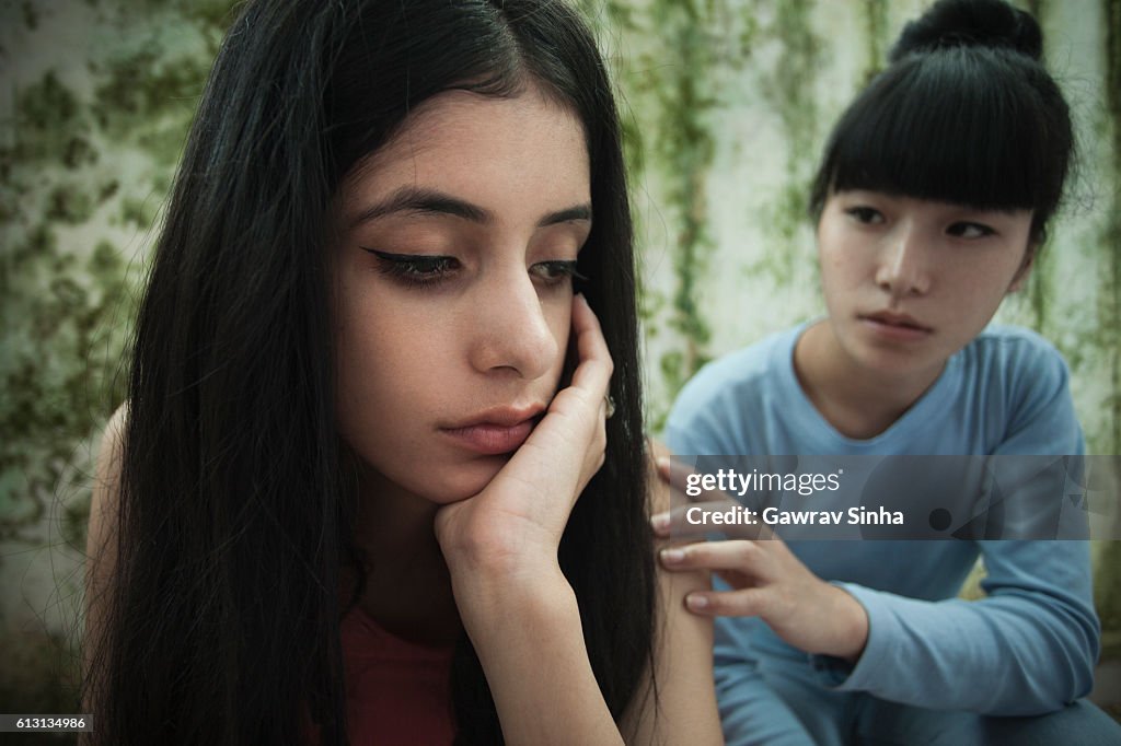 Sad girl sitting hopeless and her friend giving support.