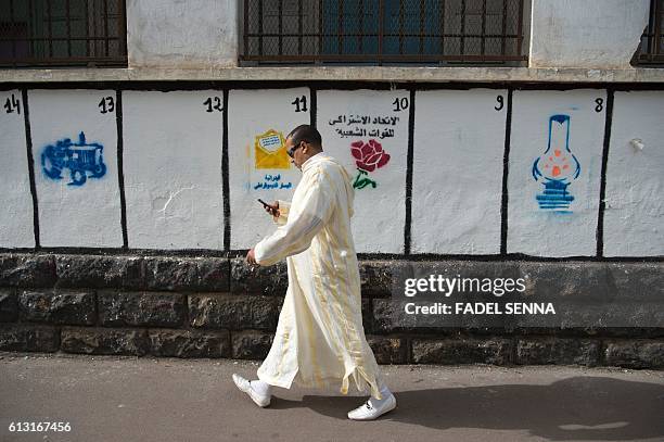 Moroccan man walks past a wall on which are painted the symbols of the political parties running for the parliamentary elections in the Moroccan...